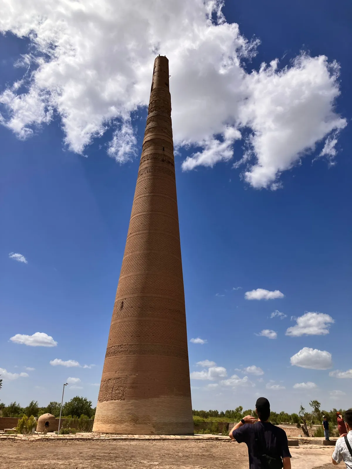 High medieval brick Kutlug Timur Minaret in Koneurgench against a blue sky with white clouds and tourists