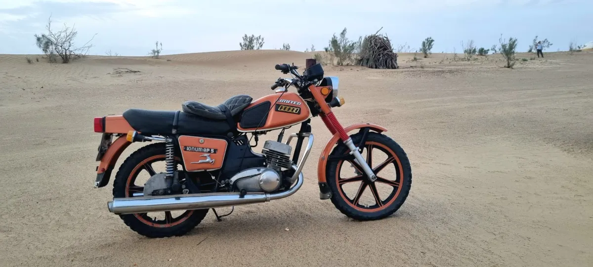 Orange Soviet retro Izh Jupiter 5 motorcycle on sand dunes in the Karakum Desert, Turkmenistan