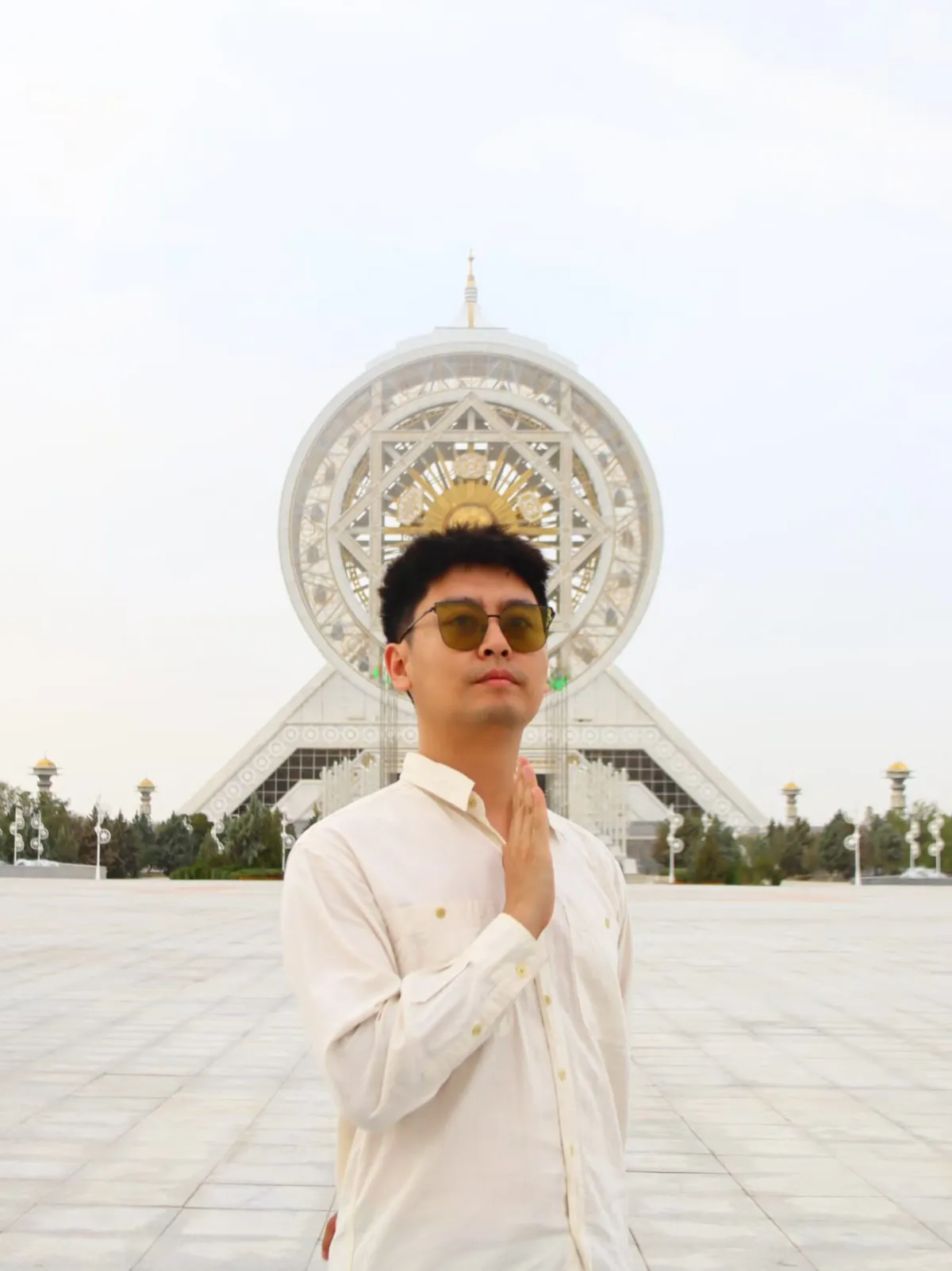 A man in sunglasses and a white shirt against the backdrop of the Alem Cultural and Entertainment Center in Ashgabat