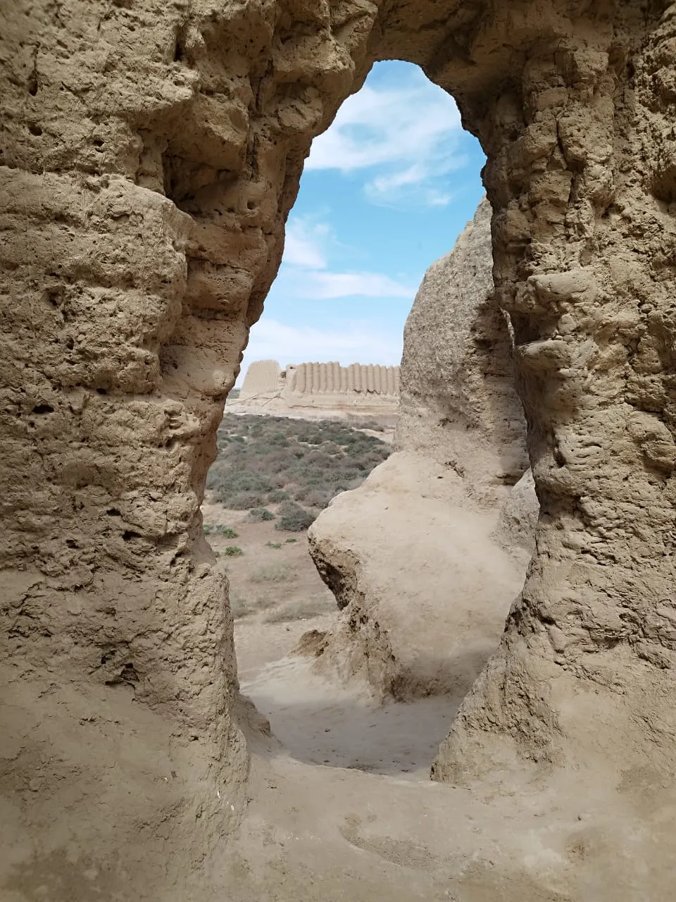A view through a clay opening in the ruins of the ancient corrugated fortress of Kyz-Kala in Merv, beneath a blue sky