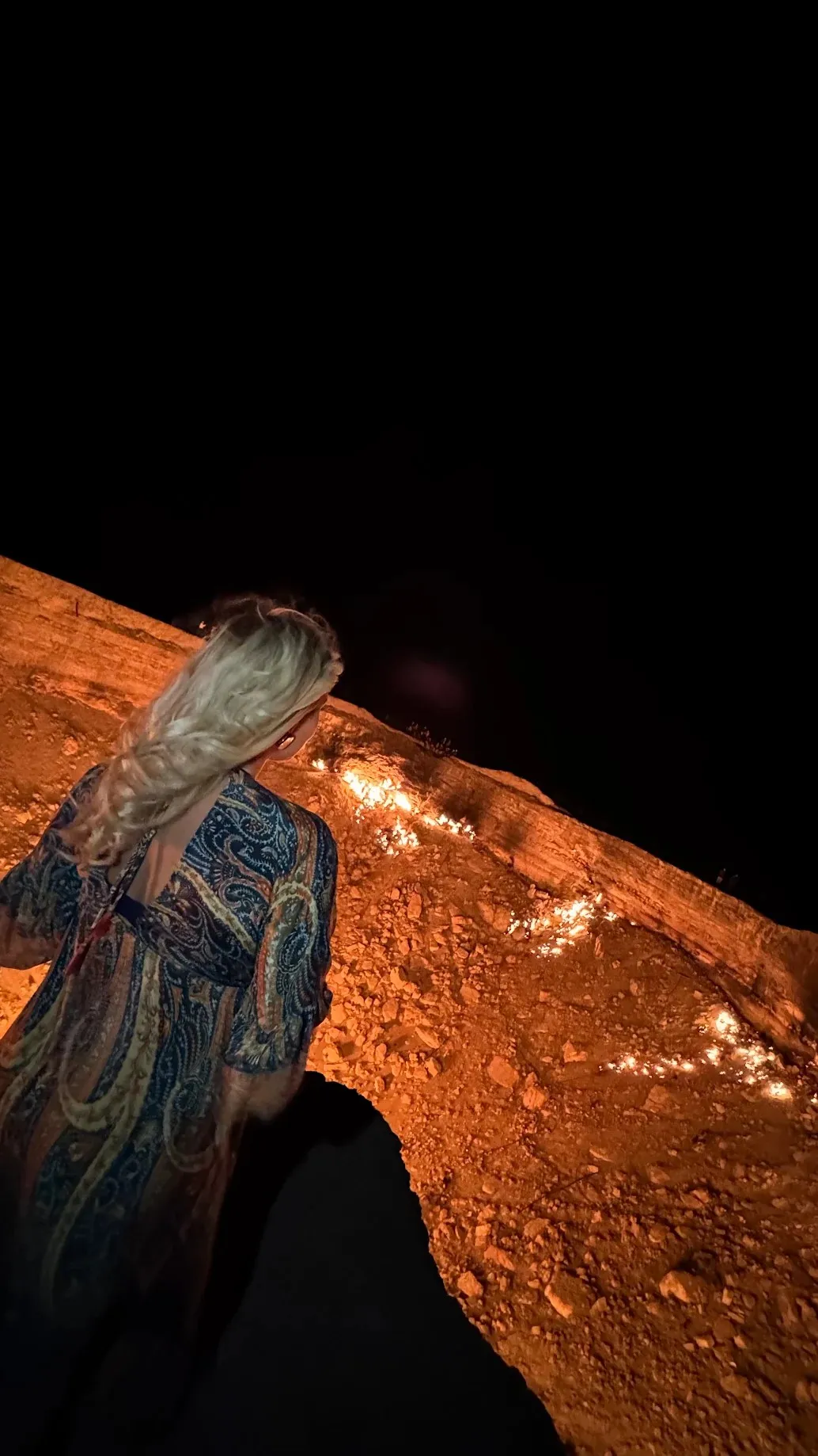 A woman at the edge of the burning Darvaza gas crater in the Karakum Desert at night
