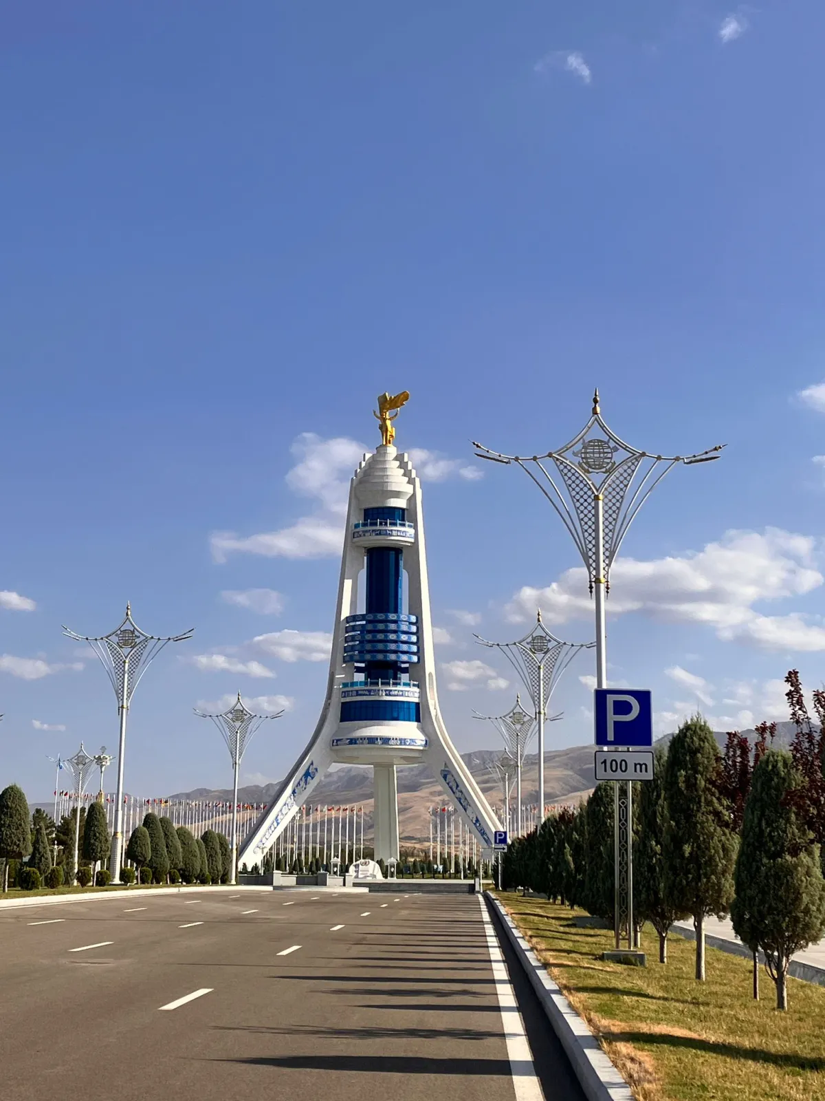 Snow-white Neutrality Monument with a golden figure on top along a wide road against the backdrop of mountains in Ashgabat