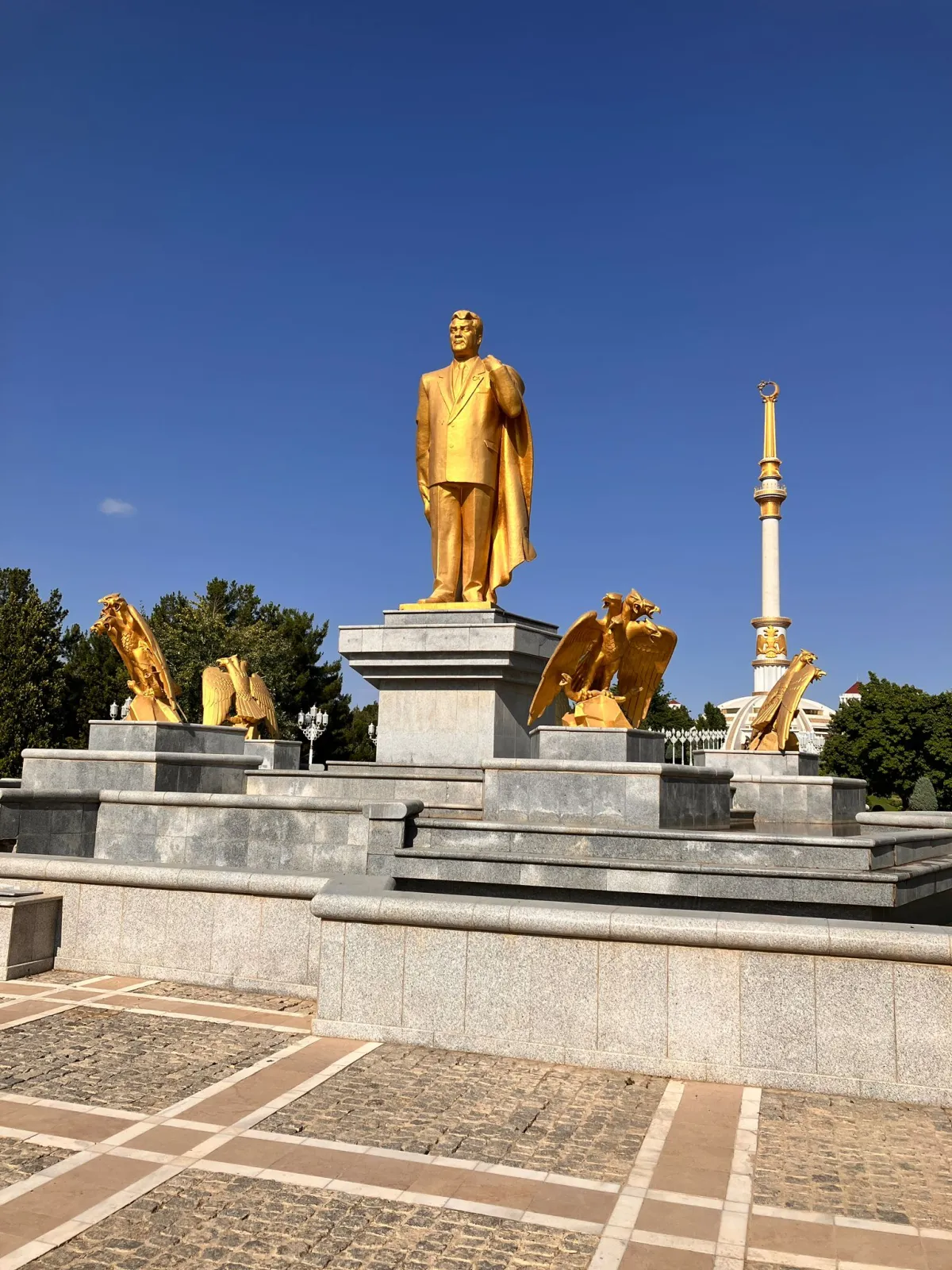 Gilded statue of Turkmenbashi surrounded by eagles against the backdrop of the Independence Monument and blue sky in Ashgabat