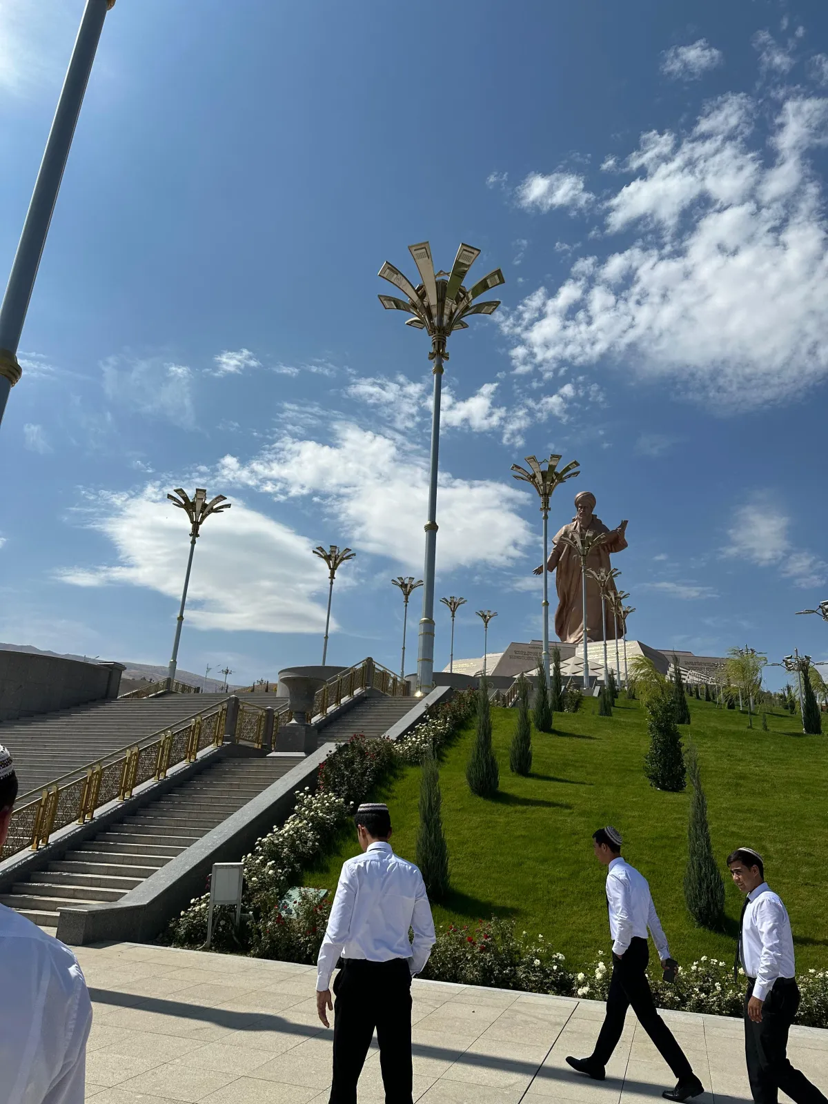 A massive bronze monument to the poet Magtymguly Pyragy on a hill with green terraces and futuristic lanterns in Ashgabat