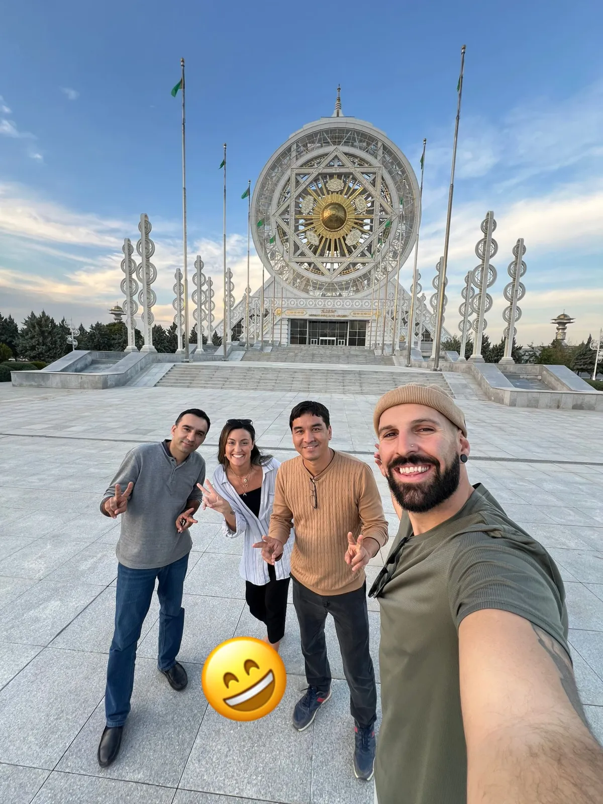 Un groupe de touristes souriants prenant un selfie devant le centre culturel et de divertissement Älem à Achgabat